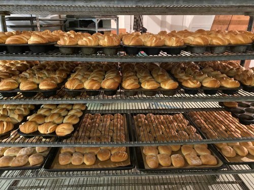 Freshly baked rolls arranged on multiple shelves in a bakery, showcasing a variety of shapes and sizes.