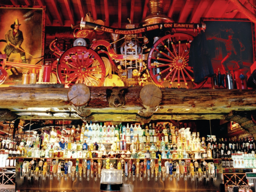 A vibrant bar scene featuring a vintage fire truck, colorful bottles, and rustic wooden decor.