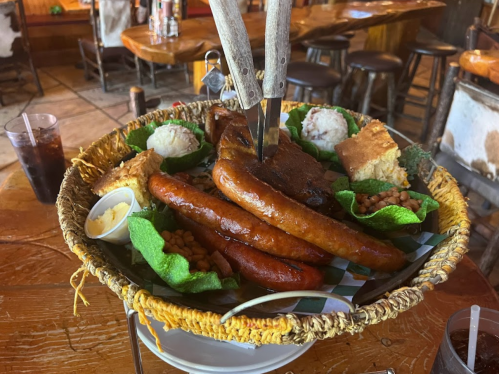 A woven basket filled with various meats, cornbread, beans, and sides, served in a rustic dining setting.