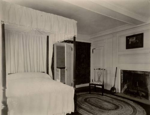 A vintage bedroom featuring a four-poster bed, a fireplace, and a round rug on the wooden floor.