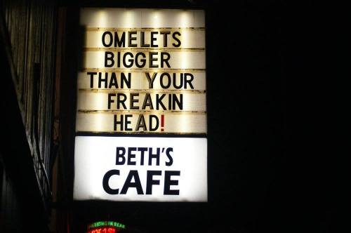 Sign for Beth's Cafe at night, advertising "Omelets bigger than your freakin head!" in bold letters.