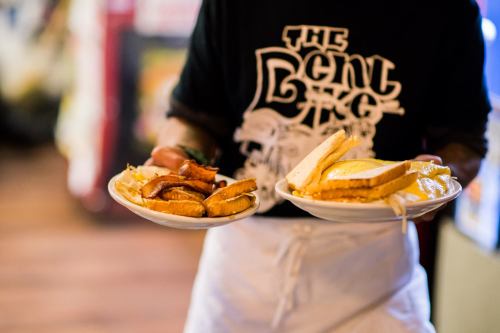 A server holds two plates of food, one with fried items and the other with a sandwich and melted cheese.