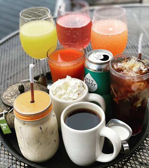 A variety of colorful drinks on a table, including cocktails, iced coffee, and a cup of hot coffee with whipped cream.