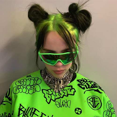 A person with green hair styled in buns, wearing oversized green sunglasses and a graffiti-patterned sweatshirt.