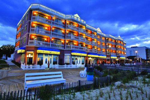 A beachfront hotel illuminated at dusk, featuring balconies and a wooden boardwalk with benches and greenery.