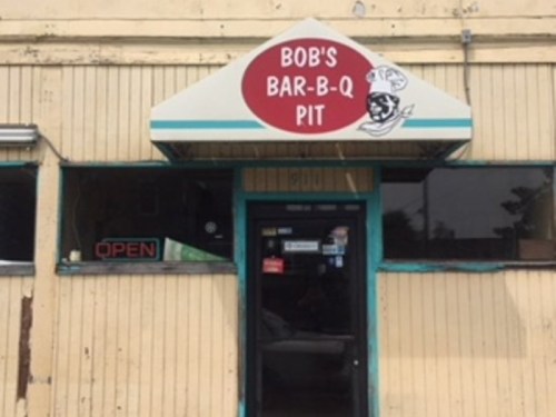 Sign for Bob's Bar-B-Q Pit, featuring a red circular logo and an open sign on the door of a rustic building.