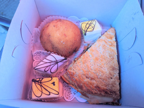 A box containing a muffin, a pastry, and two small decorated sweets on lace doilies.