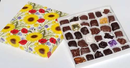 A colorful box of assorted chocolates with a floral design, partially open to reveal various chocolate pieces inside.