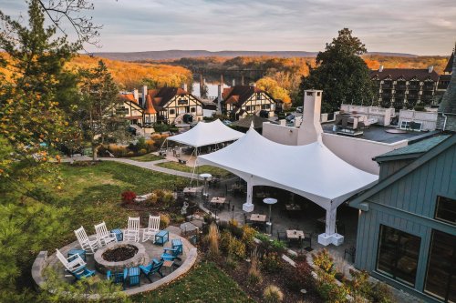 A scenic view of a resort with white tents, a fire pit, and colorful autumn foliage in the background.