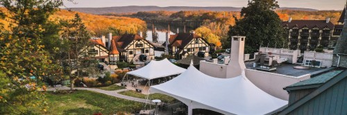 A scenic view of a resort with white tents, surrounded by autumn trees and hills in the background.