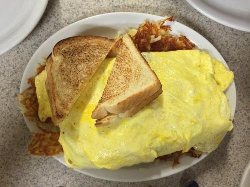 A large omelet on a bed of hash browns, served with two slices of toasted bread on a white plate.