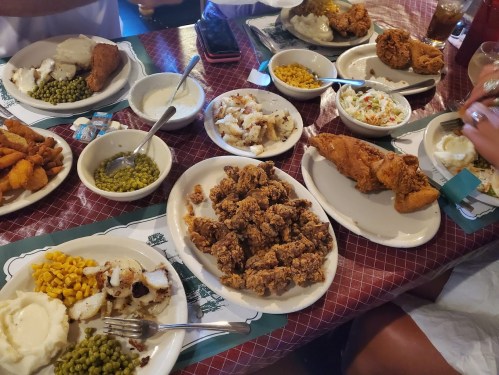 A table filled with various dishes, including fried chicken, mashed potatoes, corn, coleslaw, and green peas.