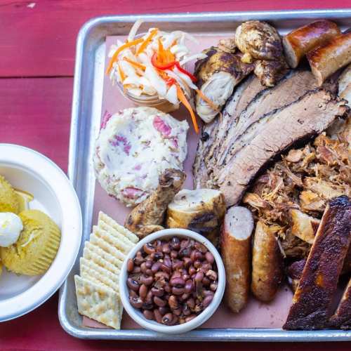 A platter of assorted barbecue meats, sides, and crackers, including brisket, sausage, pulled pork, and coleslaw.