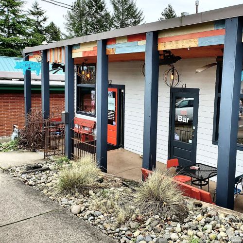 Exterior view of a small bar with colorful accents, outdoor seating, and a landscaped pathway.