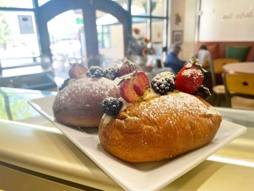 Two sweet pastries topped with strawberries and blackberries, dusted with powdered sugar, on a white plate.