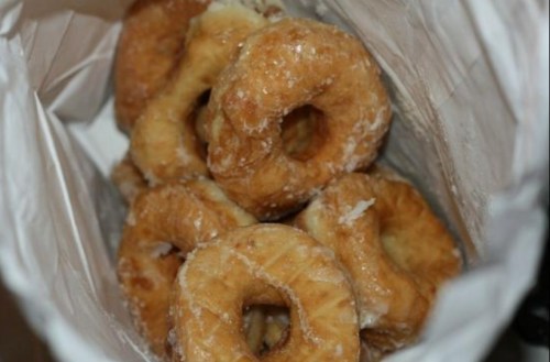 A bag filled with several glazed donuts, showcasing their golden-brown color and sugary coating.