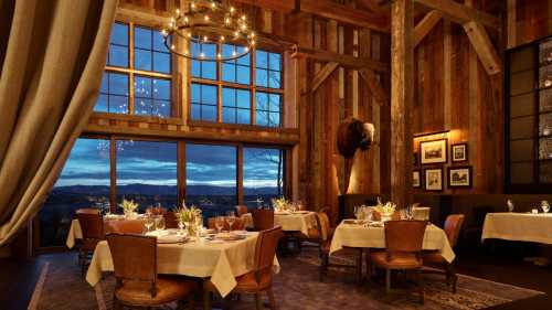 Cozy restaurant interior with wooden beams, elegant tables, and large windows showcasing a sunset view.