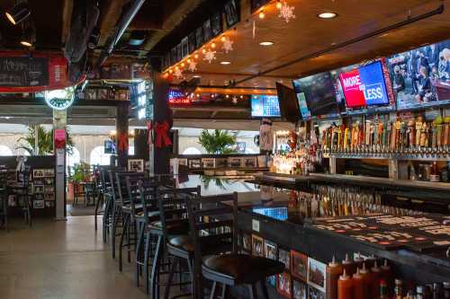 A lively bar interior with a long counter, numerous beer taps, festive decorations, and a TV displaying a news broadcast.