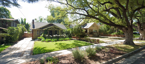A sunny street view of two charming houses with lush lawns and large trees, creating a peaceful neighborhood atmosphere.
