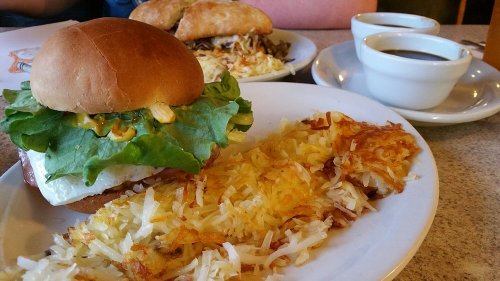 A plate featuring a sandwich with lettuce, a side of crispy hash browns, and two small cups of dipping sauce.