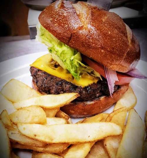 A juicy cheeseburger with lettuce, tomato, and pickles, served with golden fries on a white plate.