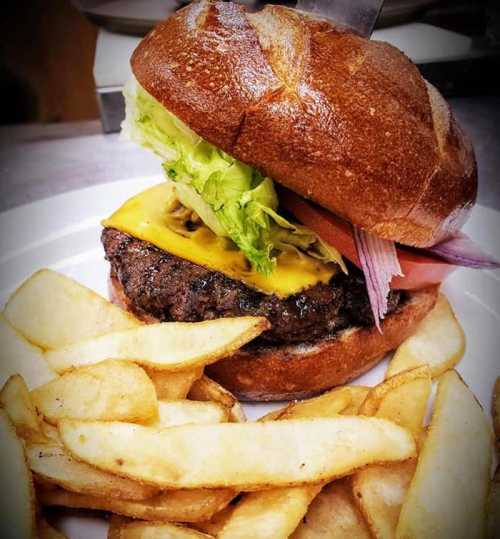 A juicy cheeseburger with lettuce, tomato, and pickles, served with golden fries on a white plate.