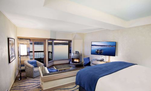 Cozy hotel room with a lake view, featuring a TV, seating area, and a fireplace. Bright and inviting atmosphere.