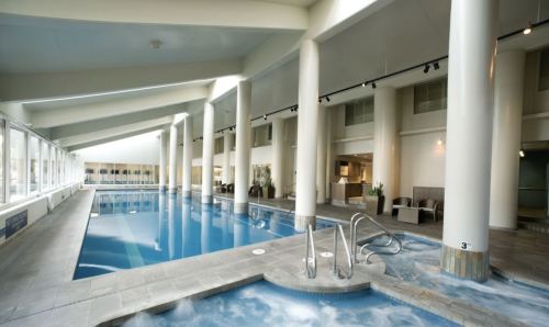 Indoor swimming pool with large windows, modern design, and a hot tub area. Bright and spacious atmosphere.