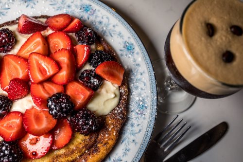 A plate of pancakes topped with strawberries and blackberries, alongside a glass of creamy coffee dessert.