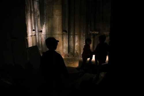 Silhouettes of children exploring a dimly lit stone chamber, with light illuminating the walls.