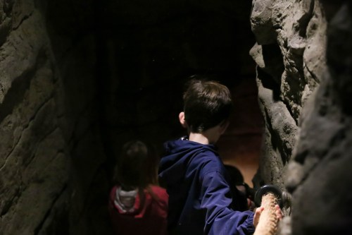 A child in a blue jacket descends a rocky tunnel, with another child visible in the background.