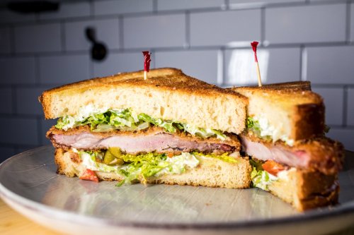 A close-up of a sliced sandwich with layers of lettuce, tomato, pickles, and thick bacon on toasted bread.