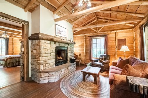 Cozy cabin interior with wooden beams, stone fireplace, comfortable seating, and a warm, inviting atmosphere.