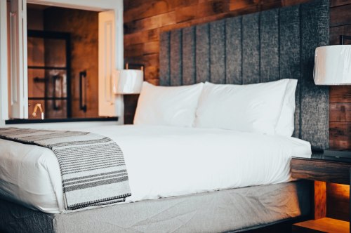 Cozy hotel room featuring a neatly made bed with gray headboard and striped throw blanket, warm lighting, and wooden accents.