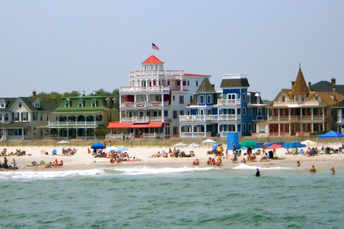 Colorful beach houses line the shore, with people relaxing on the sand and umbrellas dotting the beach.