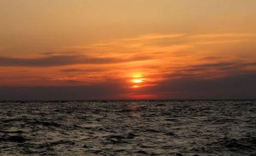 A serene sunset over the ocean, with vibrant orange and yellow hues reflecting on the water's surface.