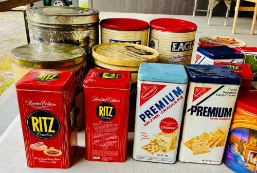 A collection of vintage cracker and cookie tins in various colors and designs, including Ritz and Premium brands.