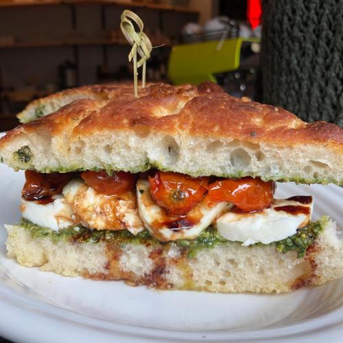 A close-up of a sandwich with pesto, mozzarella, and roasted tomatoes on crusty bread, garnished with a toothpick.