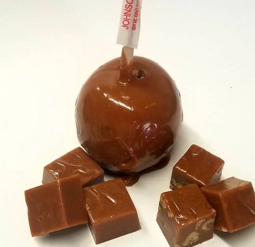 A chocolate-covered caramel apple with a stick, surrounded by small caramel cubes on a white background.
