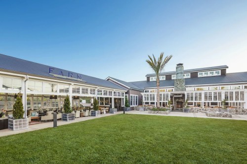 A modern restaurant with a spacious outdoor area, featuring large windows, a stone fireplace, and palm trees.