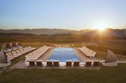 A serene pool area with lounge chairs, surrounded by lush hills and a sunset in the background.