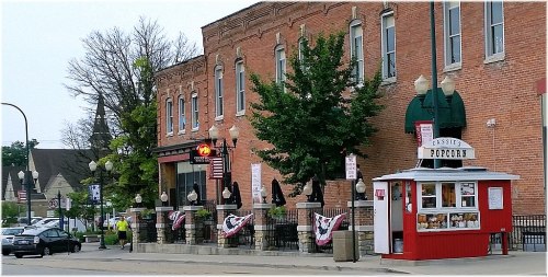 A street view of a brick building with a popcorn stand, trees, and decorative flags in a small town setting.
