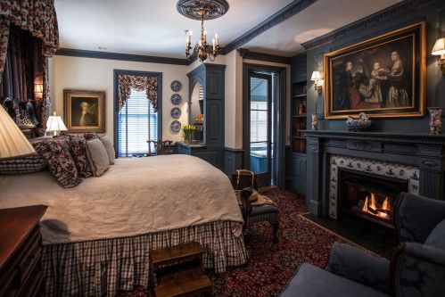Cozy bedroom with a large bed, elegant decor, fireplace, and classic artwork, featuring rich colors and textures.