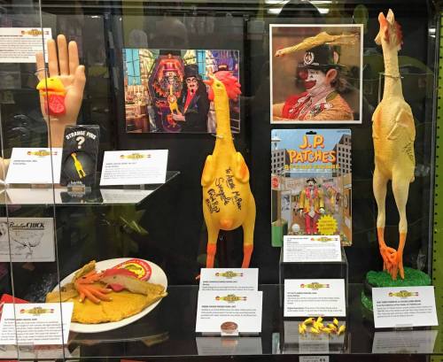 Display case featuring quirky chicken-themed items, including toys, memorabilia, and a colorful poster.