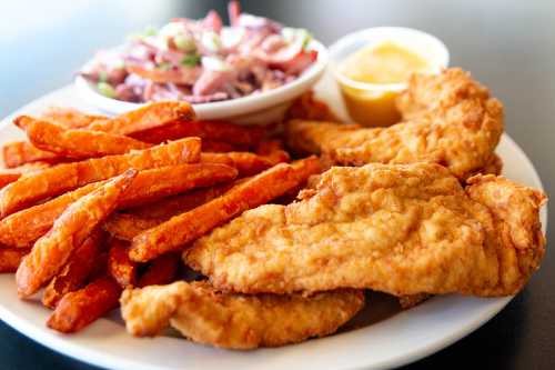 A plate of crispy fried fish fillets, sweet potato fries, and a side of coleslaw with dipping sauce.