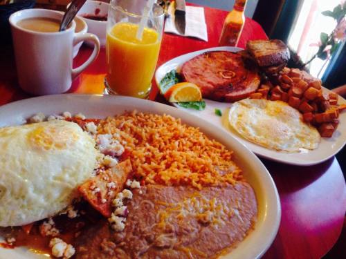 A colorful breakfast spread featuring eggs, rice, beans, ham, toast, and a glass of orange juice.