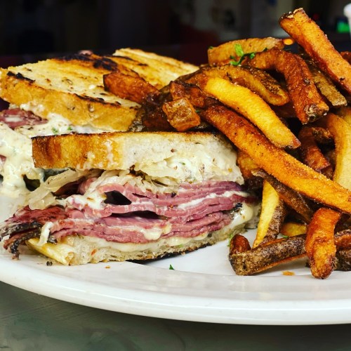 A close-up of a sandwich with layers of meat and cheese, served with a side of crispy French fries.