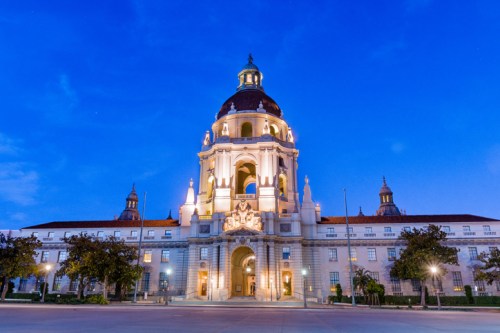Historic building with a dome, illuminated at dusk, surrounded by trees and a clear blue sky.