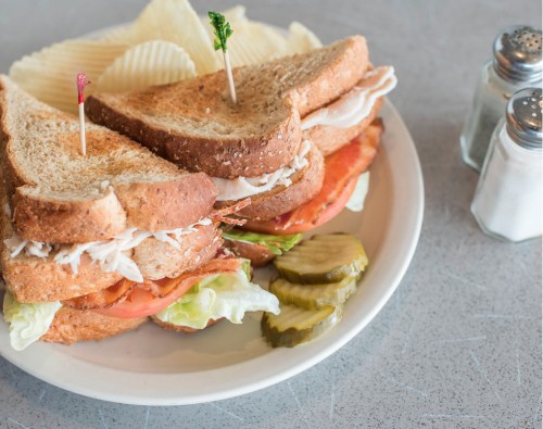 A plate with a stacked sandwich, lettuce, tomato, pickles, and potato chips, garnished with toothpicks.