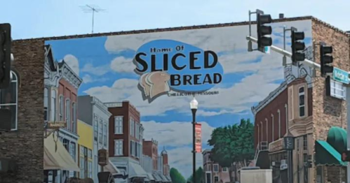 Mural on a building featuring the text "Home of Sliced Bread" with a blue sky and street scene below.